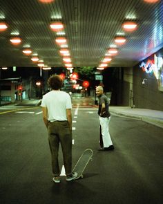 two men are standing on the street with their skateboards