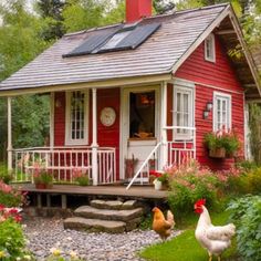 two chickens are standing in front of a small red house with a porch and steps leading up to it