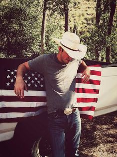 a man leaning on the back of a truck with an american flag draped over it