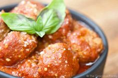 meatballs with tomato sauce and basil in a black bowl on top of a wooden table