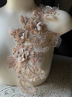 a white mannequin with flowers and lace on it's neckline, sitting on a table