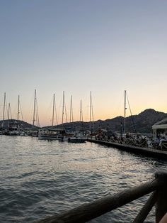 many sailboats are docked in the water near a pier at sunset or dawn with mountains in the background