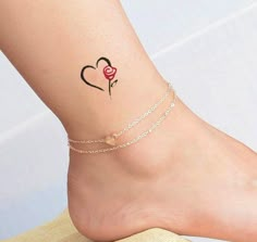 a small tattoo on the ankle of a woman with a heart and flower in it