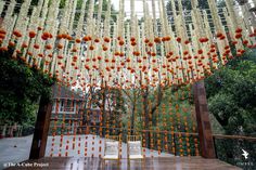 an outdoor wedding venue with orange and white flowers hanging from the ceiling, surrounded by trees