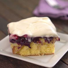 a piece of cake with white frosting and blueberry topping on a square plate