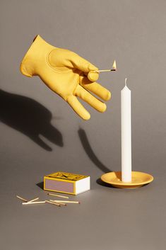 a hand in yellow gloves is lighting a candle with a match on a plate next to matches