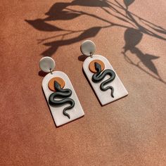 two pairs of earrings with black and orange designs on them sitting on a brown surface