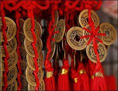 red and gold decorations hanging from hooks with chinese writing on them, along with coins