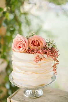 a white cake topped with pink flowers on top of a wooden table next to a tree