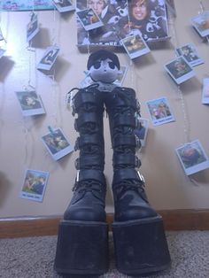 a pair of black boots sitting in front of a wall with pictures hanging on it