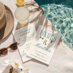 the wedding stationery is laid out next to the swimming pool and sunhats