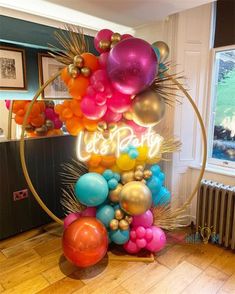 there is a large balloon arch in the room with balloons all over it and a neon sign that says let's party