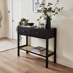 a black console table with plants and books on it in front of a white door