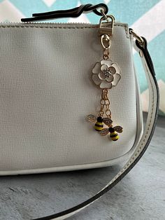 a white purse with a bee charm hanging from it's front pocket, on a table