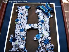 the letter h is made up of paper flowers and leaves, with blue accents on it