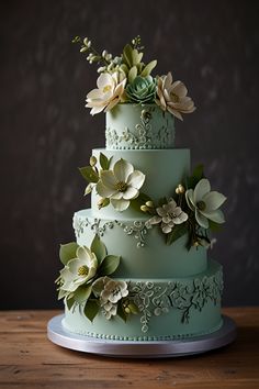 a three tiered green wedding cake with flowers on the top and sides, sitting on a wooden table