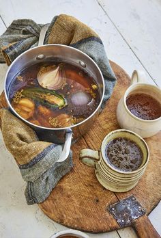 a pot filled with soup sitting on top of a wooden cutting board next to two mugs