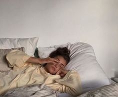 a woman is laying in bed with her eyes closed and she has one hand on her head