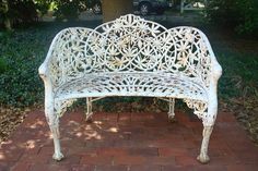 a white metal bench sitting on top of a brick walkway in front of a tree