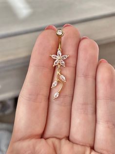 a hand holding a gold and white diamond flower brooch or earring in it's left hand