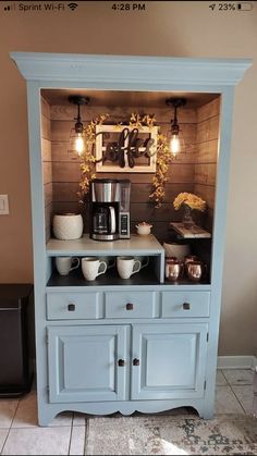 a blue hutch with coffee maker and cups on it's side, sitting in front of a brown wall