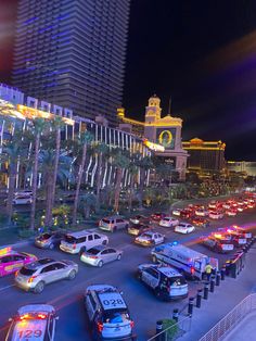 a busy street filled with lots of traffic next to tall buildings and palm trees at night