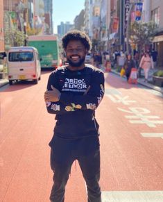 a man standing in the middle of a street with his arms crossed and smiling at the camera