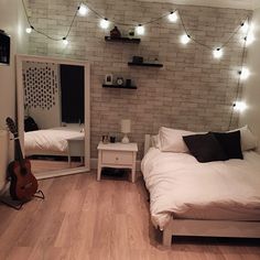 a bedroom with white brick walls and string lights strung over the bed, along with a guitar