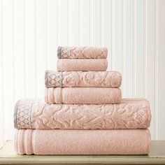 a stack of pink towels sitting on top of a wooden table next to a white wall