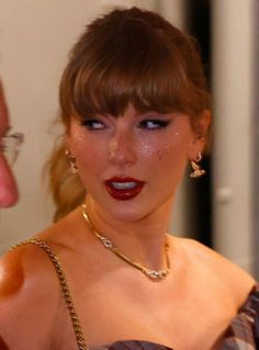 a woman in a dress with red lipstick on her face and gold jewelry around her neck