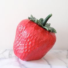 a red ceramic strawberry sitting on top of a marble counter