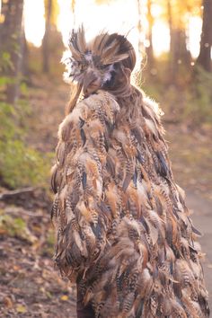 a woman walking in the woods with lots of feathers on her coat and hair pulled back