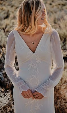 a woman wearing a white dress standing in the desert with her hands on her hips