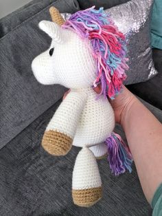 a crocheted unicorn stuffed animal sitting on top of a couch next to a person's hand