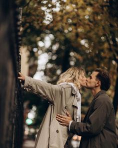 a man and woman kissing on the street with trees in the backgrouf