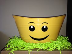 a yellow pot with green grass around it and a smiley face painted on the side