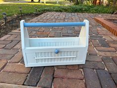 a white basket with blue handles sitting on top of a brick walkway next to a park