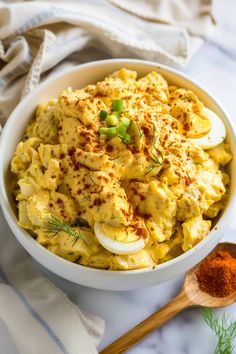 a bowl filled with macaroni and cheese on top of a table next to a wooden spoon