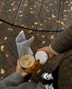 two people holding cups of coffee and croissants in their hands while sitting on the ground