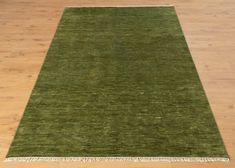 a green rug with fringes on top of a wooden floor in an empty room