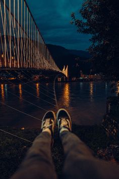 someone's feet are standing in front of a bridge at night