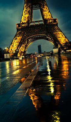 the eiffel tower is lit up at night with its reflection in the wet pavement