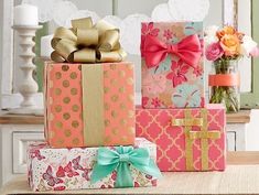 three colorful boxes with bows on them sitting on a table next to flowers and candles