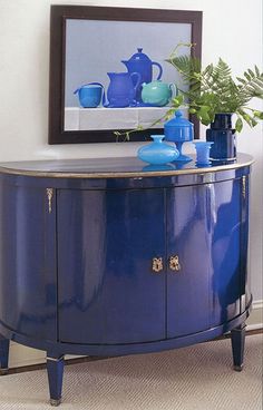 a blue sideboard with vases and plants on it in front of a mirror