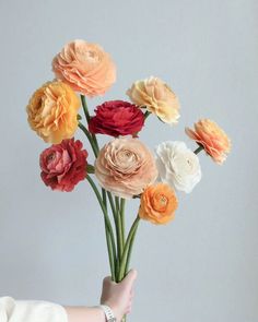 a hand holding a bunch of paper flowers in it's right hand, with the top one being held up