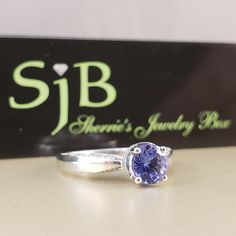 "Tanzanite Statement Ring This beautiful 6 millimeter Tanzanite, set in a unique 4-prong halo Engagement Style mounting. A solid 10kt White Gold Ring with accents of Genuine White Diamonds on both sides of the Ring and under the center stone, giving the look of a crown. The diamond accents equalling .24 carat total weight. For those who appreciate the nuance of color, Tanzanite is a very special, much-loved Gemstone that comes in a unique shade of Purply-Blue... very similar to one of the 2016 C Tanzanite Gemstone With Center Stone As Gift, Tanzanite Gemstones Perfect For Gifts, Classic Tanzanite Gemstones For Anniversary, Brilliant Cut Tanzanite Gemstones For Gift, Brilliant Cut Tanzanite Gemstones As Gift, Tanzanite Amethyst Birthstone Ring For Anniversary, Anniversary Tanzanite Birthstone Ring, Classic Tanzanite Solitaire Sapphire Ring, Classic Sapphire Tanzanite Solitaire Ring