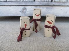 three snowmen made out of wooden blocks with red ribbon tied around the faces and nose