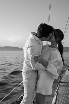 a man and woman kissing on the deck of a sailboat at sunset in black and white