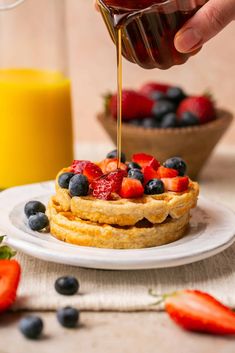 someone drizzling syrup onto a waffle topped with strawberries and blueberries