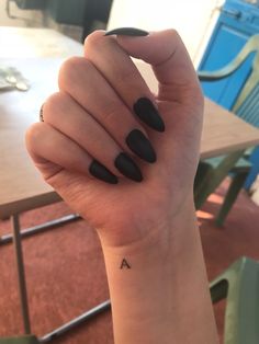 a woman's hand with black nails and a small tattoo on her left wrist